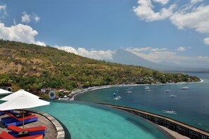 A resort with a pool, lounge chairs, and a view of the ocean and a mountain. - Zen Inn (Padangbai)