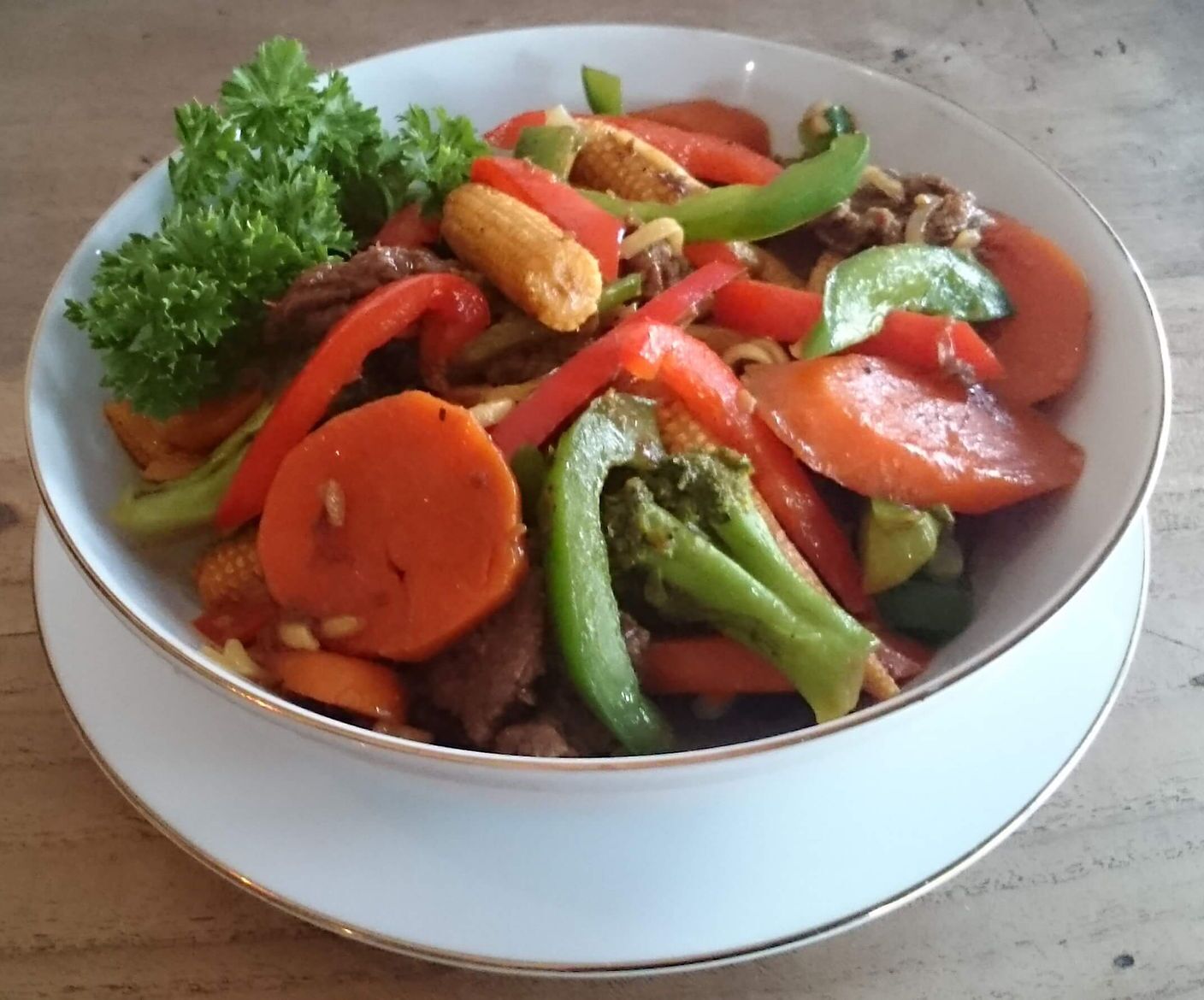 Eine Schüssel gebratenes Rindfleisch mit Gemüse, darunter Karotten, Paprika und Brokkoli, serviert auf einem weißen Teller.