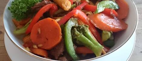 Eine Schüssel gebratenes Rindfleisch mit Gemüse, darunter Karotten, Paprika und Brokkoli, serviert auf einem weißen Teller.
