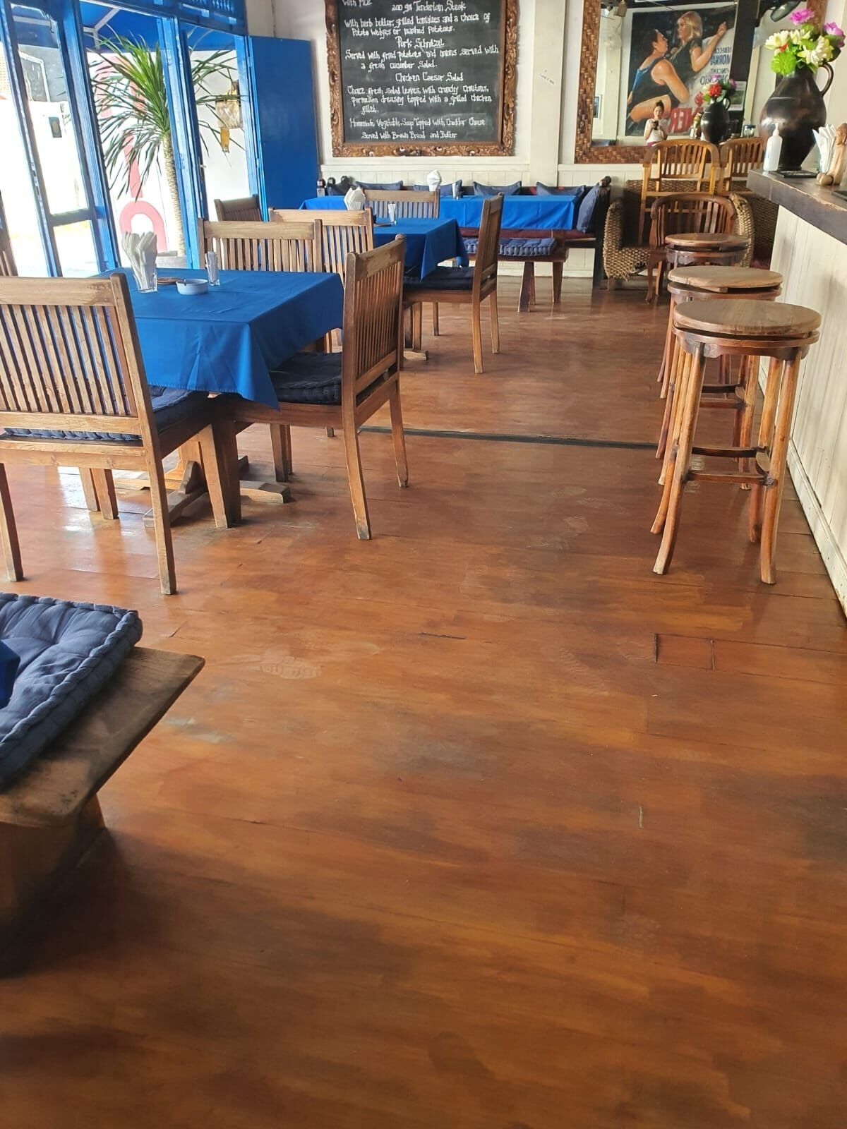 A restaurant with wooden tables and chairs, a chalkboard menu, and a blue wall.