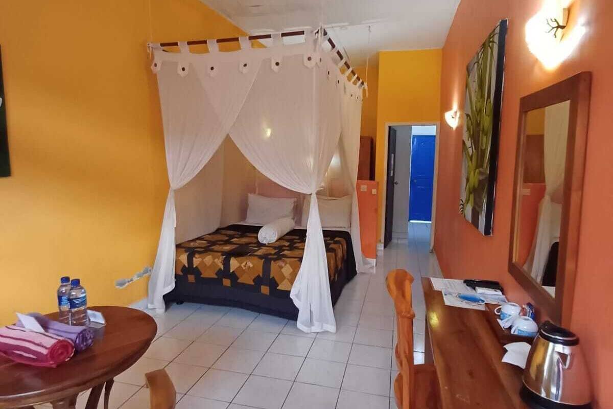 Habitación de hotel con cama, una mesa de madera, una silla, una mesita con tetera y un espejo.