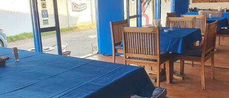 A restaurant with blue tables and chairs, a chalkboard menu, and a view of the street outside.