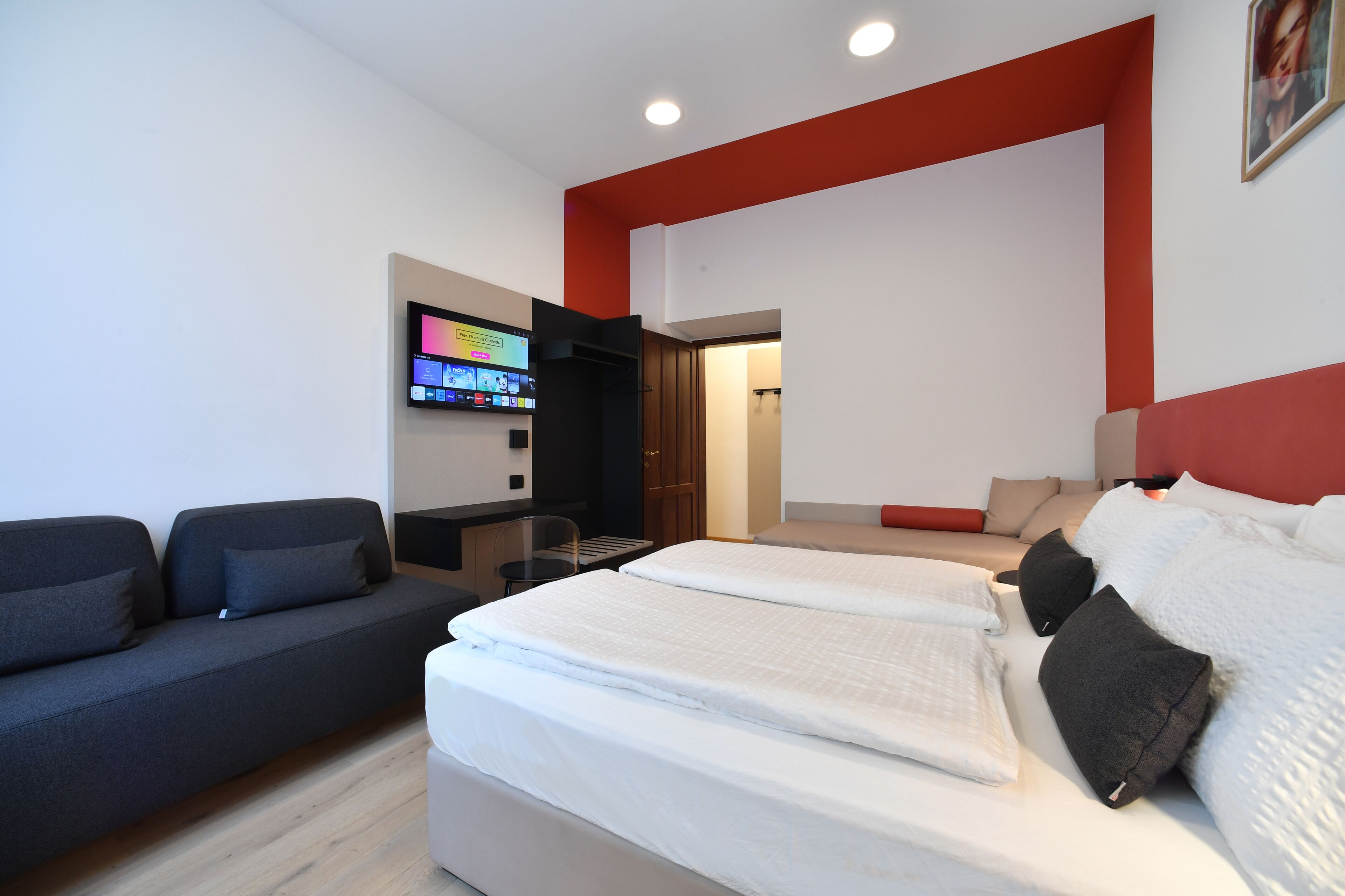 A modern hotel room with a bed, a sofa, a TV, and a desk.