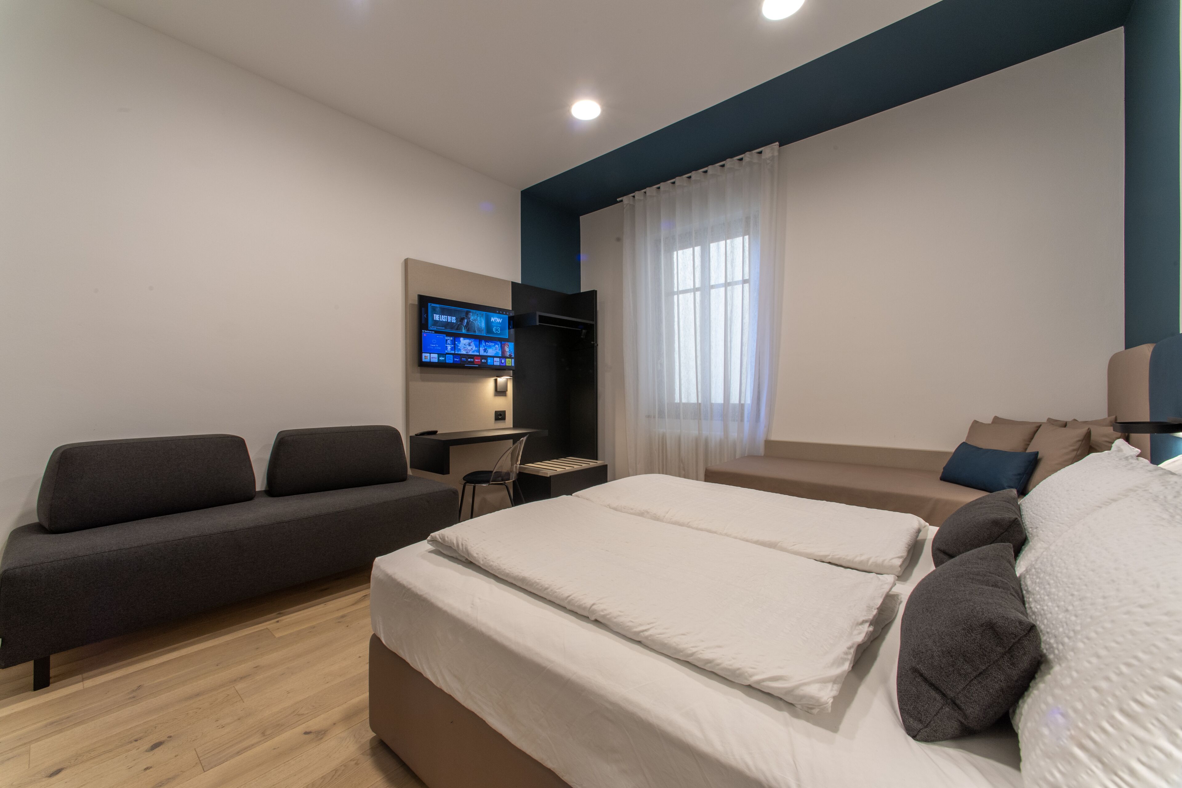 Moderni hotellihuone, jossa on sänky, sohva, työpöytä ja televisio.