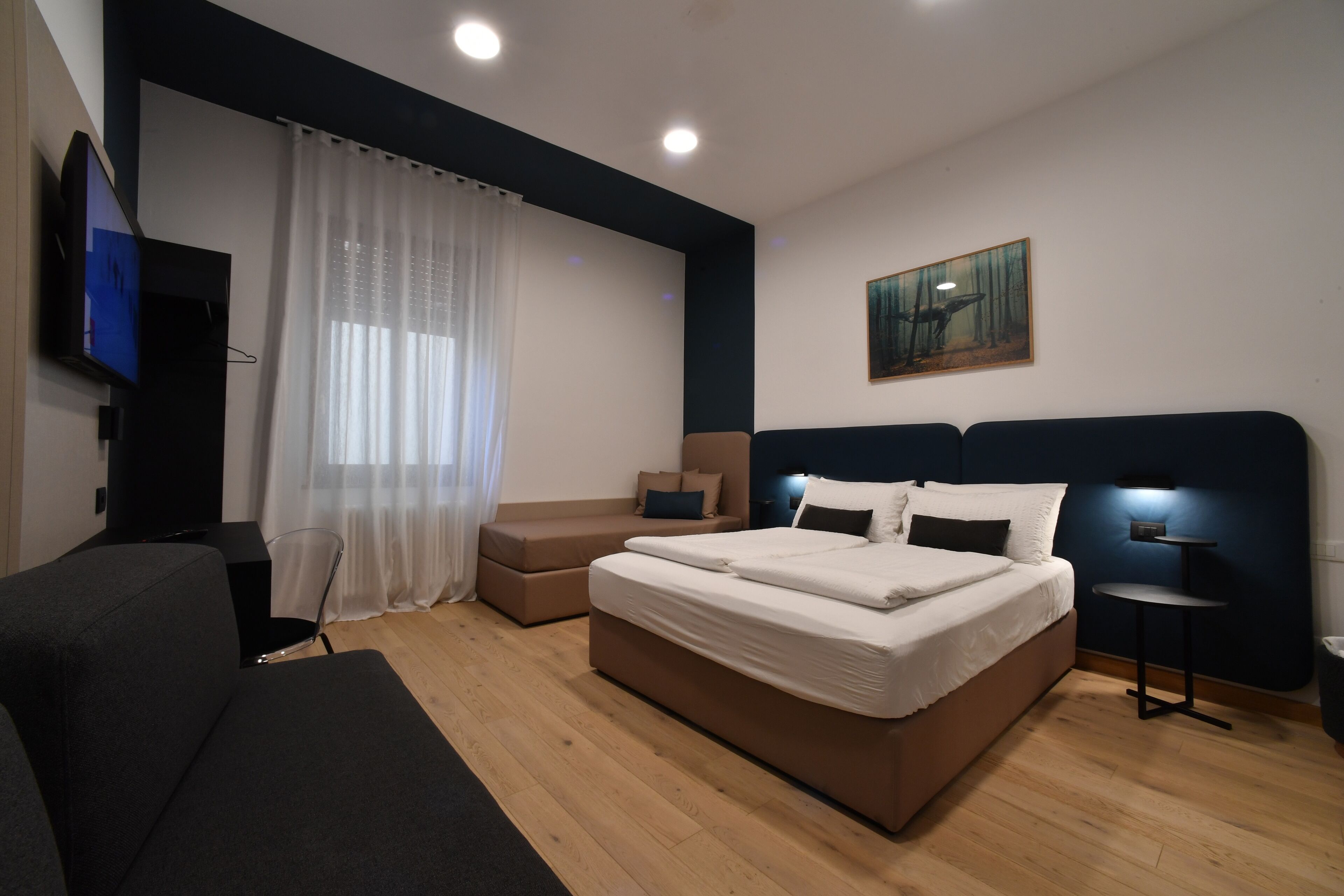 A modern bedroom with a large bed, a sofa, a TV, and a painting on the wall.