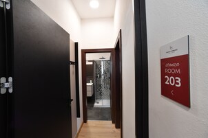 A hotel hallway leading to a bathroom with a shower and a sink. A sign indicates "Room 203" and "House of Bruno".