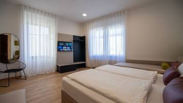Quarto de hotel moderno com uma cama grande, televisão, escrivaninha e sofá.
