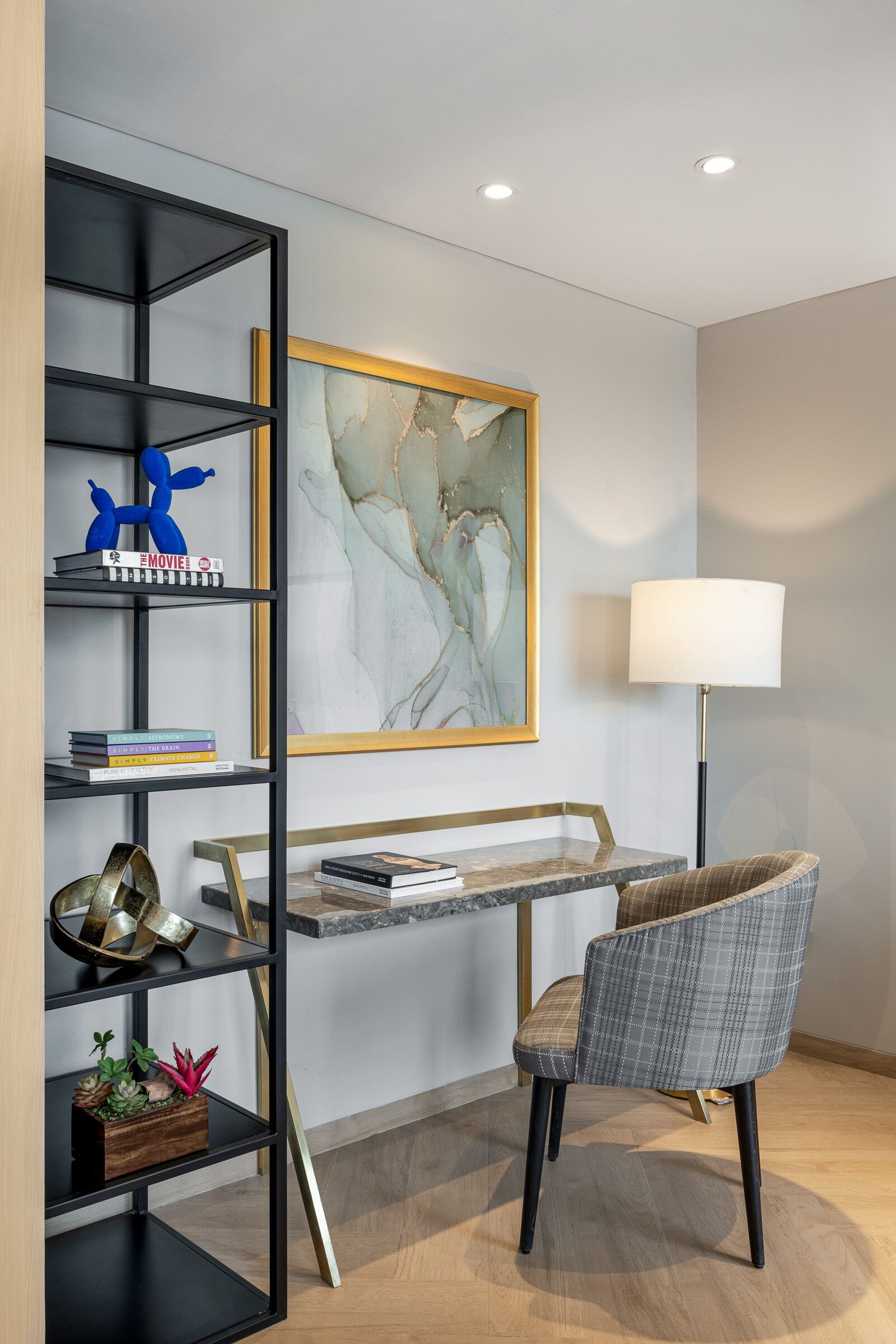 Una habitación moderna con una estantería metálica negra, un sillón de cuadros grises, un escritorio de mármol y un cuadro abstracto de gran tamaño.