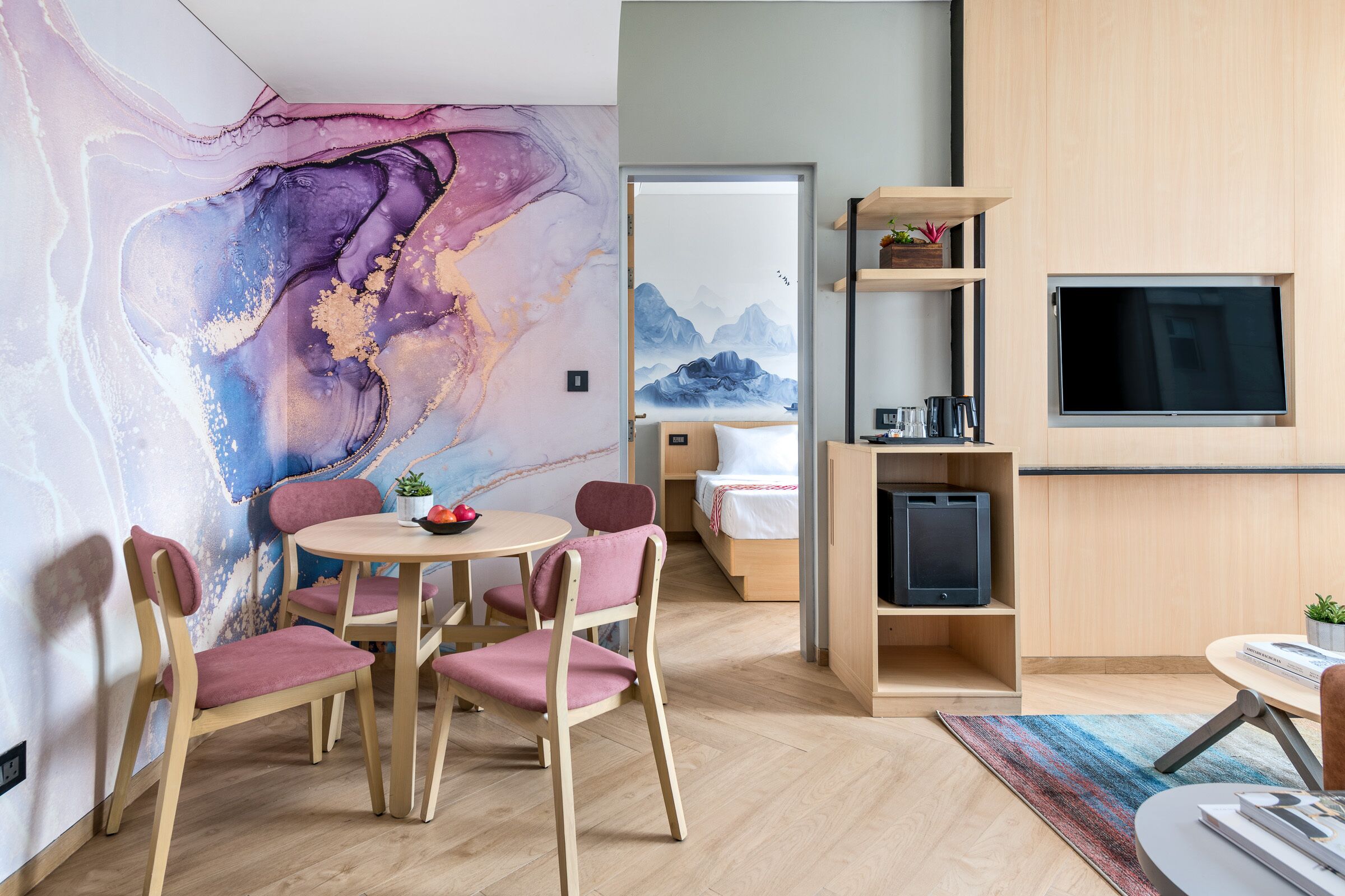 A modern room with a wooden floor, a round table with chairs, a TV mounted on the wall, and a bookshelf.