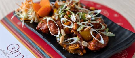 A dish with various vegetables and nuts on a black plate, placed on a colorful tablecloth with a red pattern.