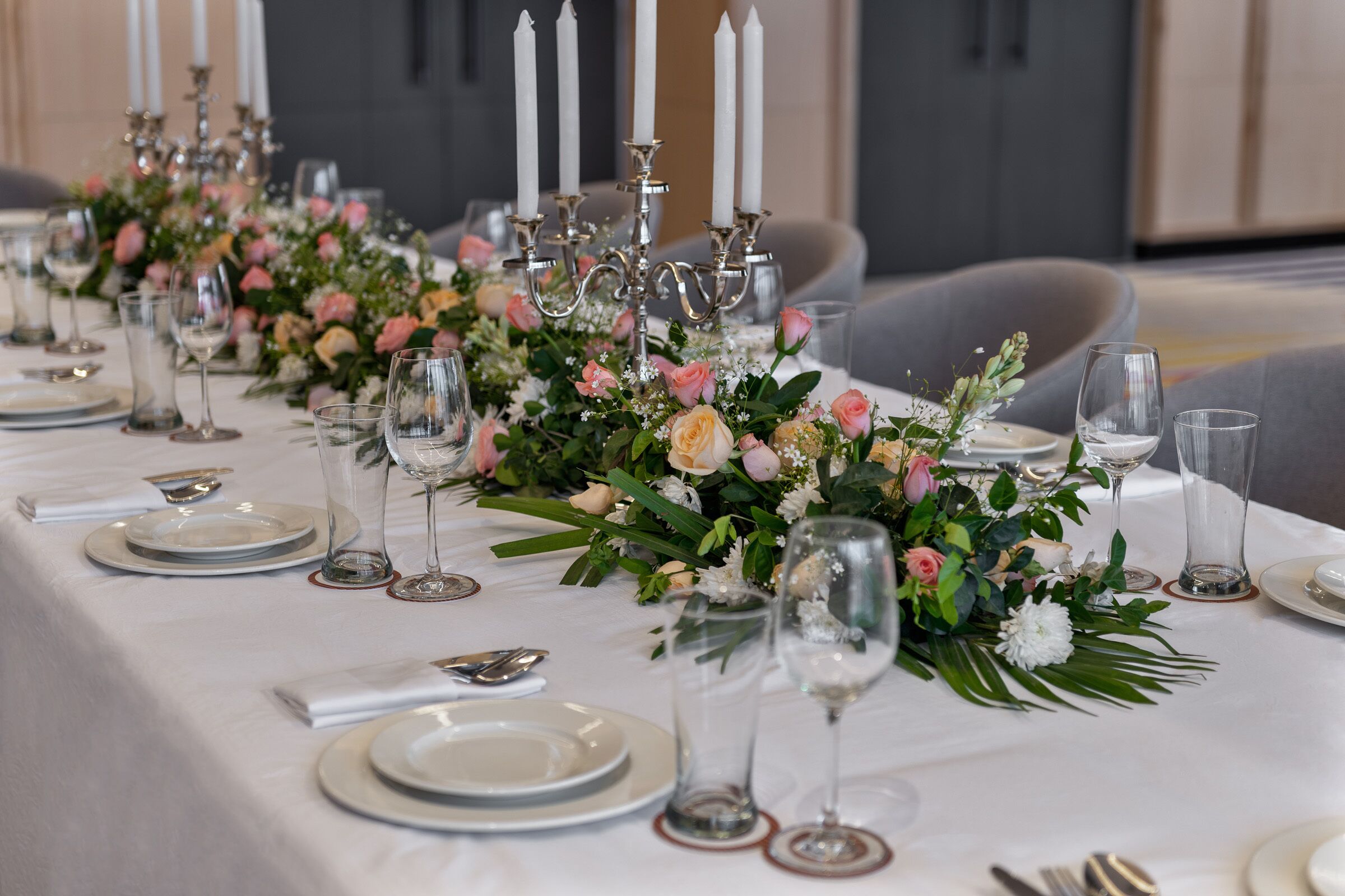 A long dining table set with white plates, clear wine glasses, and a centerpiece of flowers and greenery.