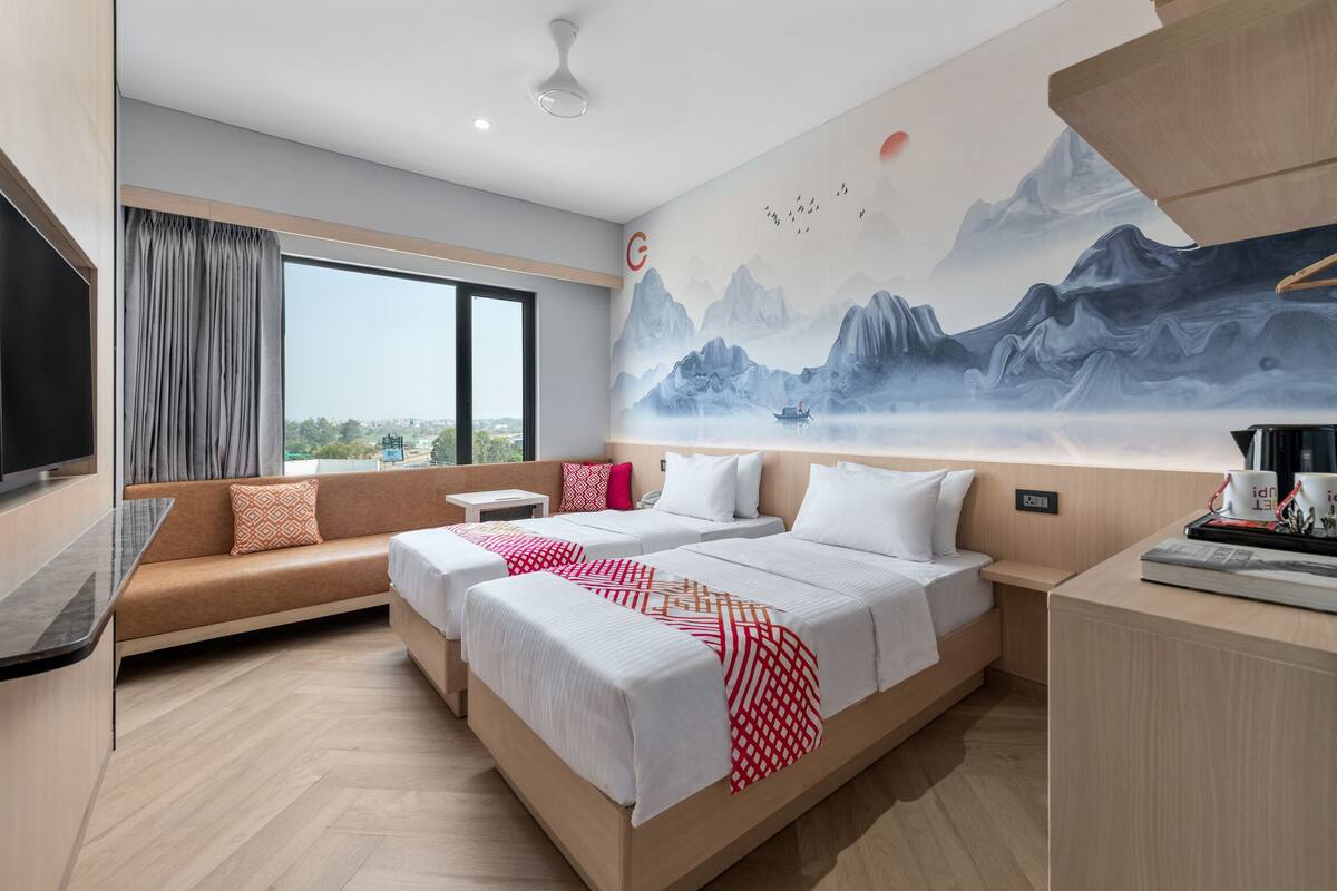 Ett modernt hotellrum med en stor säng, en soffa, en TV och en väggmålning som föreställer berg.