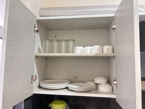 A kitchen cabinet with shelves holding plates, cups, and a green container.