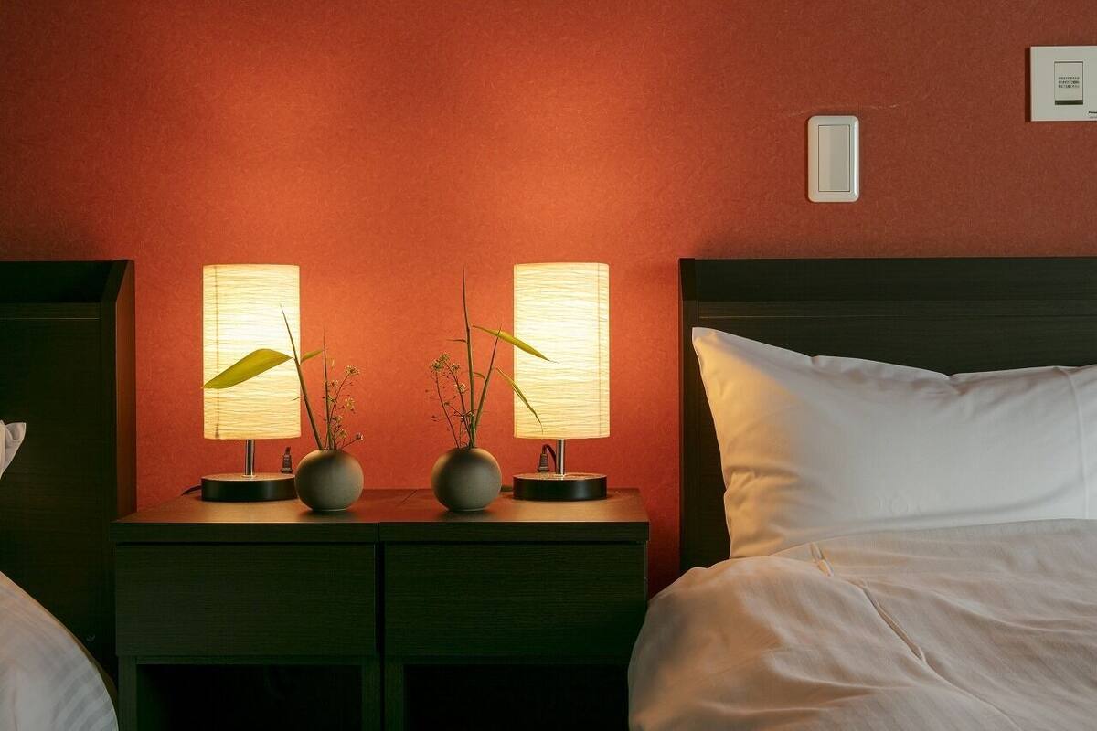 A hotel room with a bed, two bedside tables with lamps, and a wall-mounted light switch.
