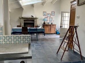 A spacious room with a tiled floor, a fireplace, a dining table with chairs, and a wooden cabinet.