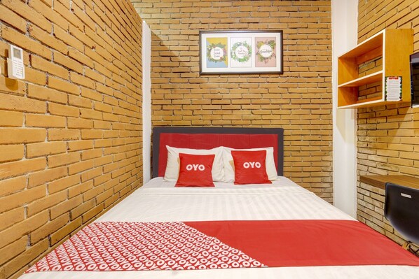Una habitación de hotel con una pared de ladrillo, una cama con ropa de cama roja y blanca, y un cuadro enmarcado sobre la cama.
