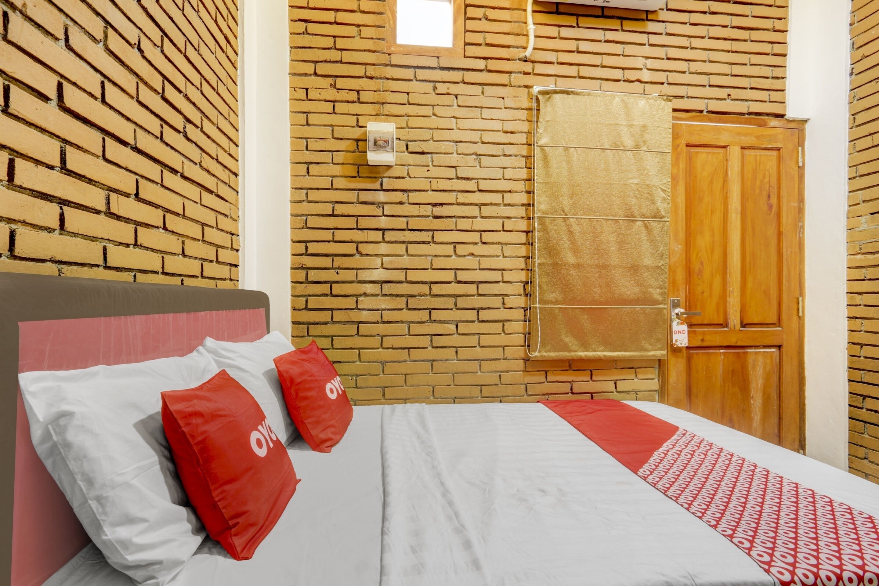 A hotel room with a brick wall, a wooden door, and a bed with red and white bedding.