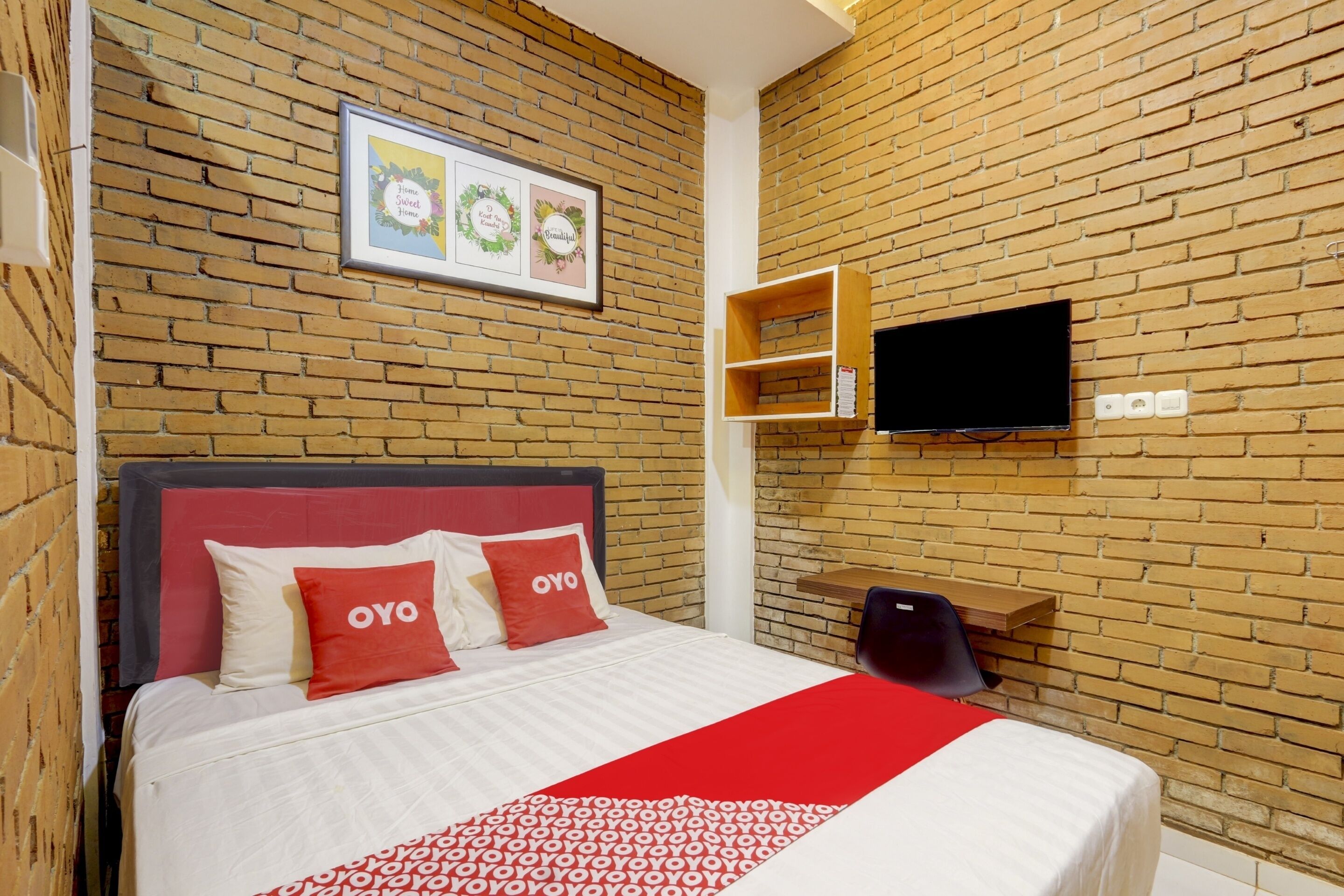 Een hotelkamer met een bakstenen muur, een bed met rode en witte beddengoed, een televisie aan de muur en een ingelijst beeld boven het bed.