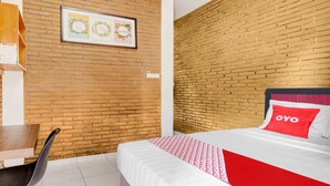 Une chambre d’hôtel avec un mur en briques, un lit recouvert d’une courtepointe rouge et blanche, un bureau en bois et une chaise.