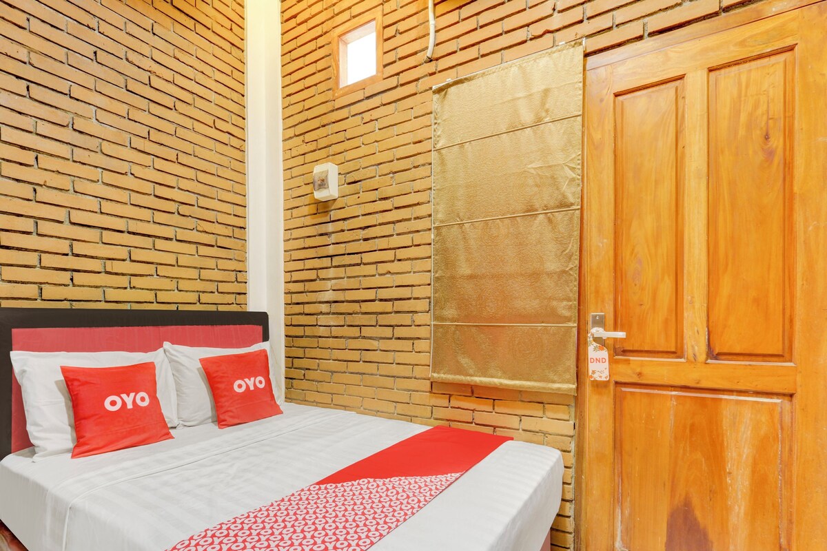 A hotel room with a brick-patterned wall, a wooden door, and a bed with red and white bedding.