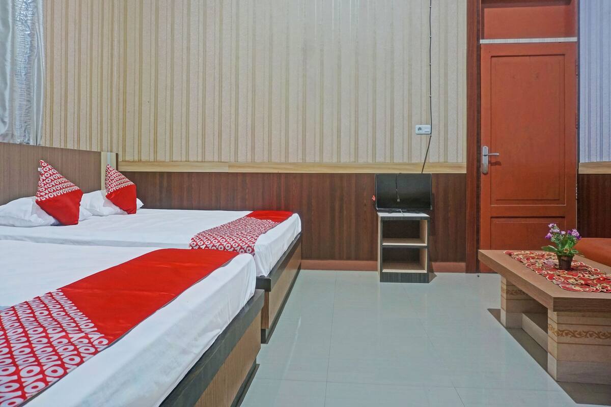 A hotel room with two beds, a wooden wardrobe, a small table with a floral arrangement, and a door.