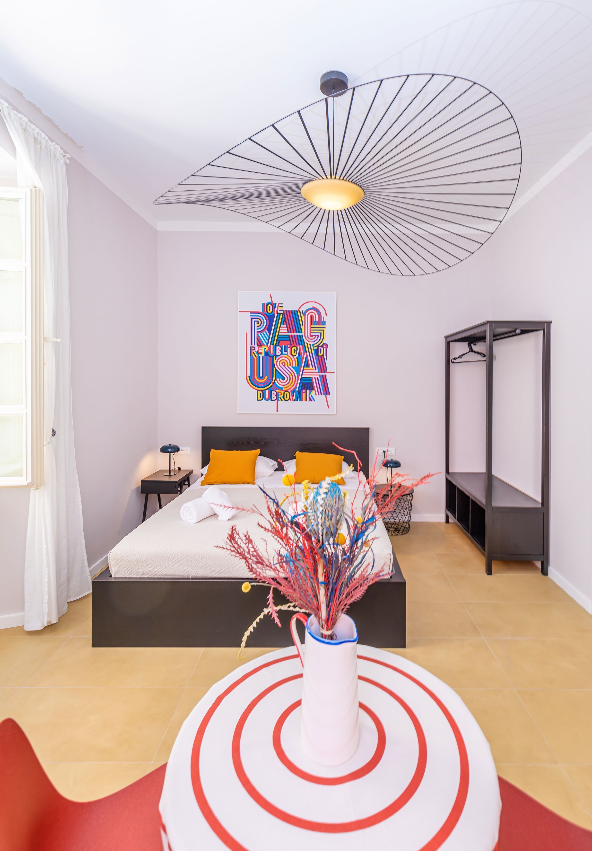 A modern bedroom with a bed, a decorative wall piece, a hanging light fixture, and a minimalist shelving unit.