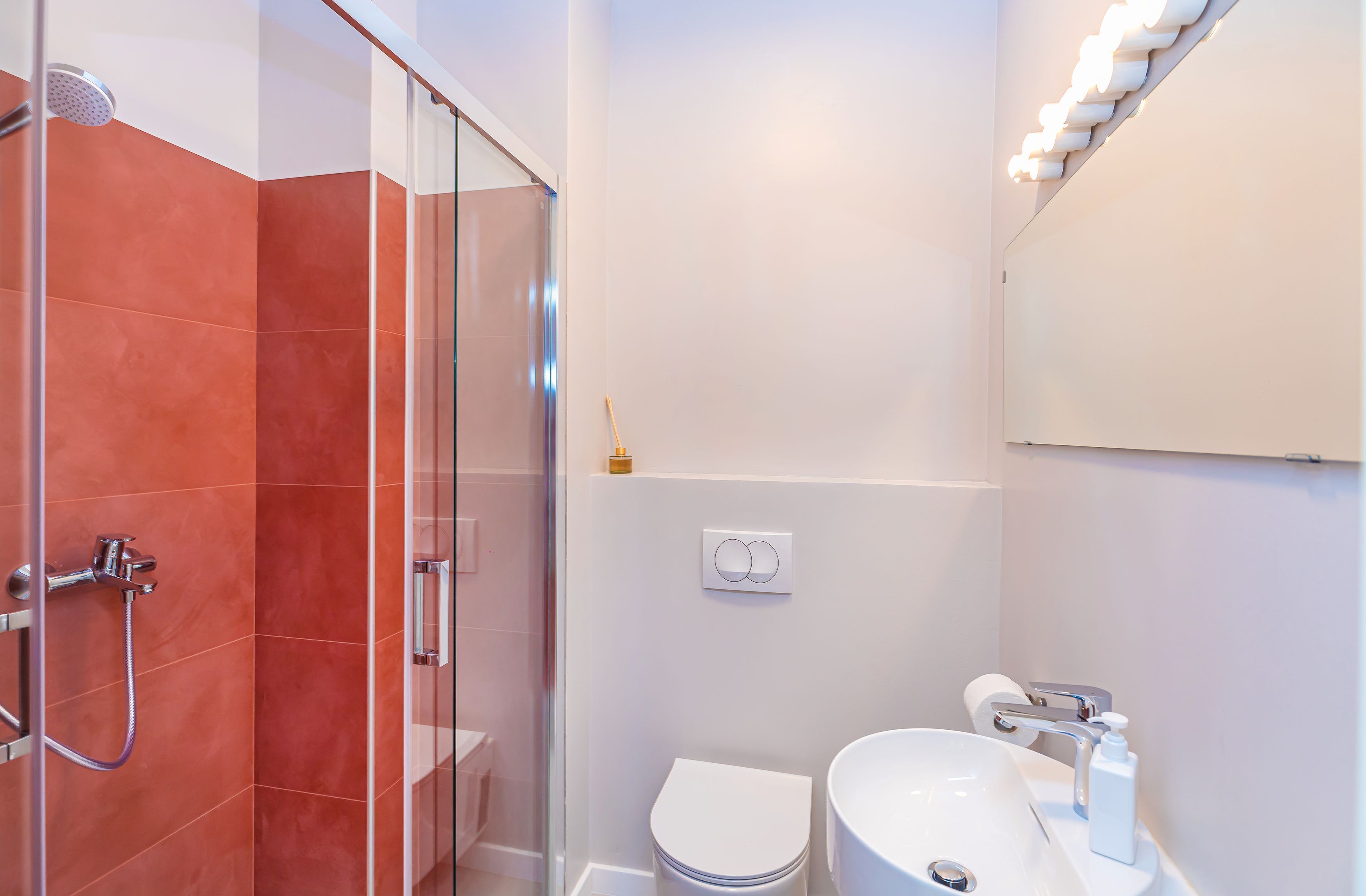 Un bany modern amb dutxa amb envàs de vidre, un vàter blanc i un lavabo amb mirall a sobre.