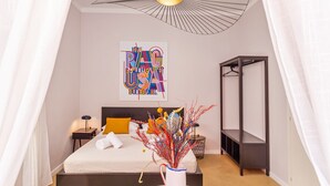 A modern bedroom with a bed, a bedside table, a hanging light fixture, a wall art piece, and a small table with chairs. - Cap rooms (Dubrovnik)