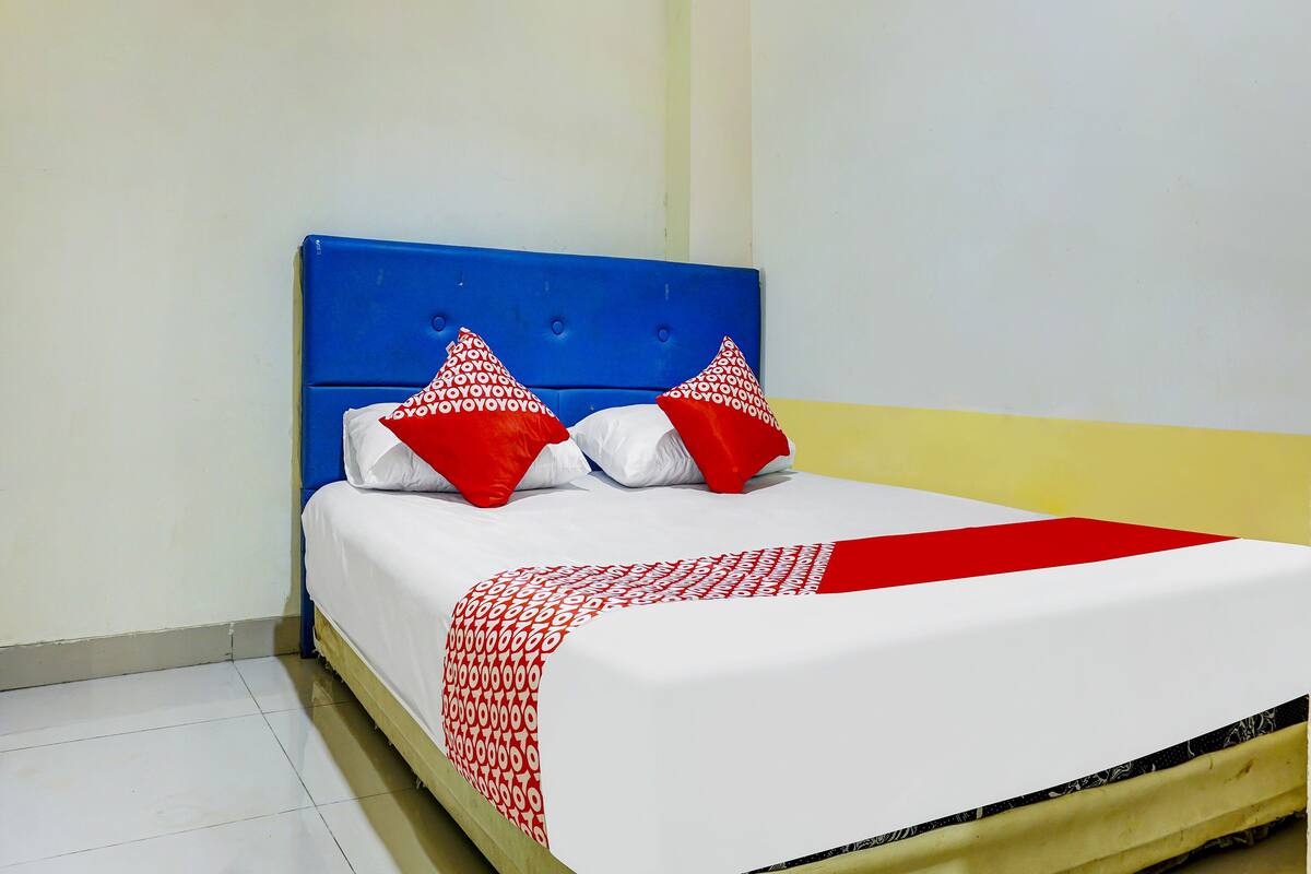 Una cama con cabecera azul, ropa de cama blanca y almohadas rojas.