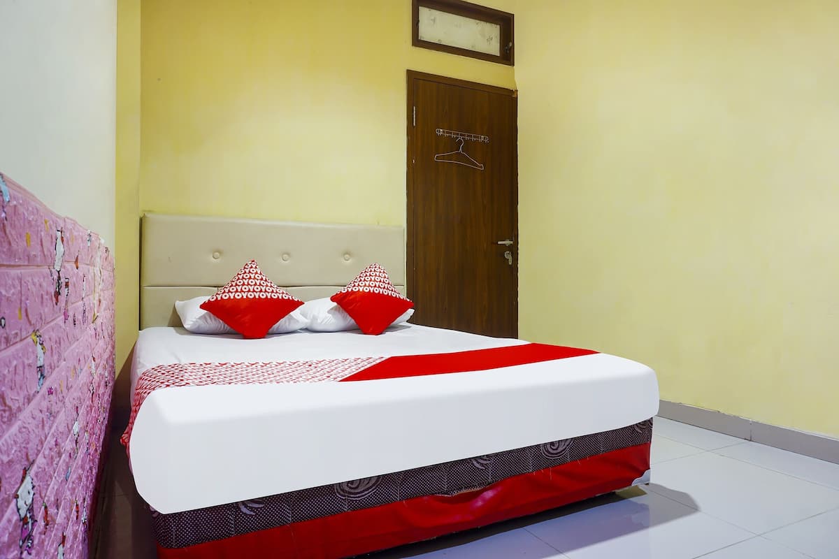 Una cama bien hecha con una colcha blanca y roja, dos almohadas rojas y blancas, y una puerta de madera con un perchero.