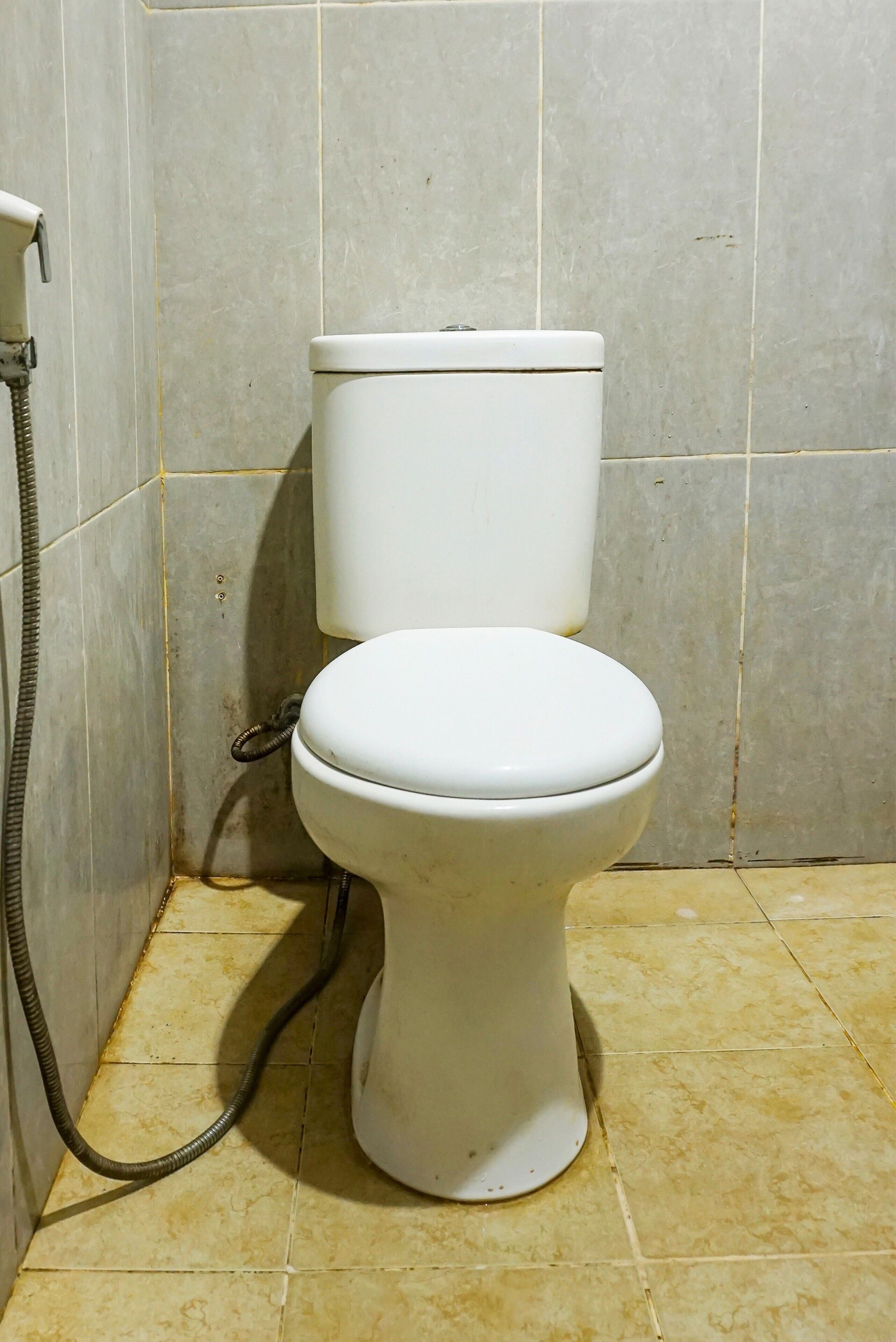 A toilet with a hose in a tiled bathroom.