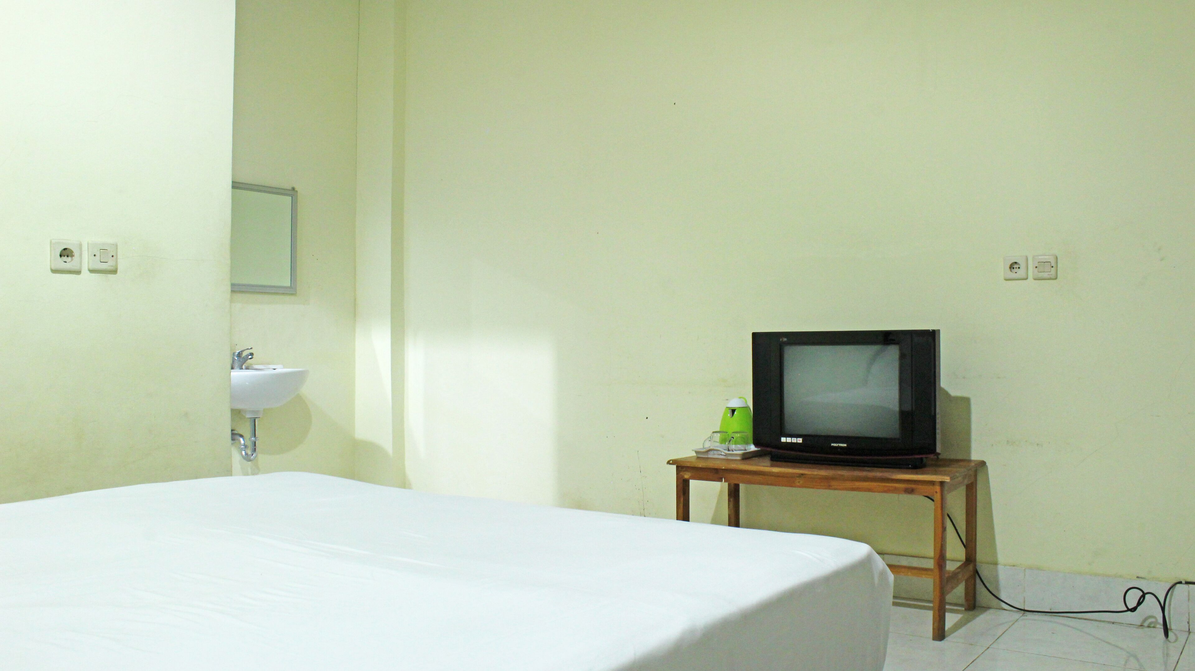 A hotel room with a bed, a small wooden table with a television, a sink, and a mirror.