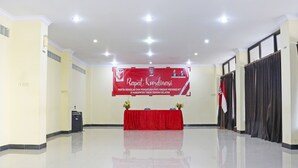 A conference room with a red banner, a podium, and a table with flowers. - Collection O 91517 Hotel Gajah Mada Soe (Soe)