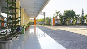 A covered outdoor area with a reflective floor, potted plants, and a clear view of the street and surrounding buildings. - Collection O 91517 Hotel Gajah Mada Soe (Soe)