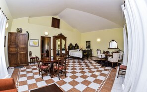 Una habitación con piso a cuadros, una mesa de comedor de madera con sillas, una cama con cabecera, un espejo y una puerta.