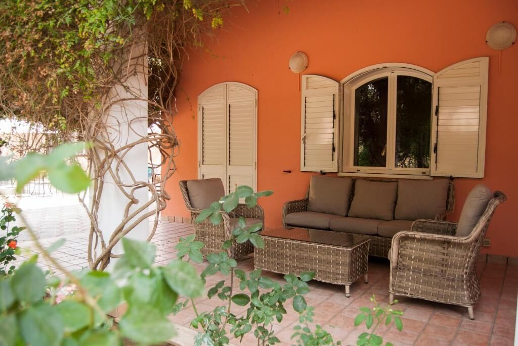 A cozy outdoor seating area with wicker furniture, a cushioned sofa, and a window with shutters.