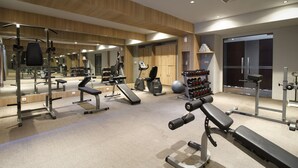 Un gimnasio moderno con diversos equipos de ejercicio, un espejo grande y vistas de la ciudad a través de amplias ventanas.