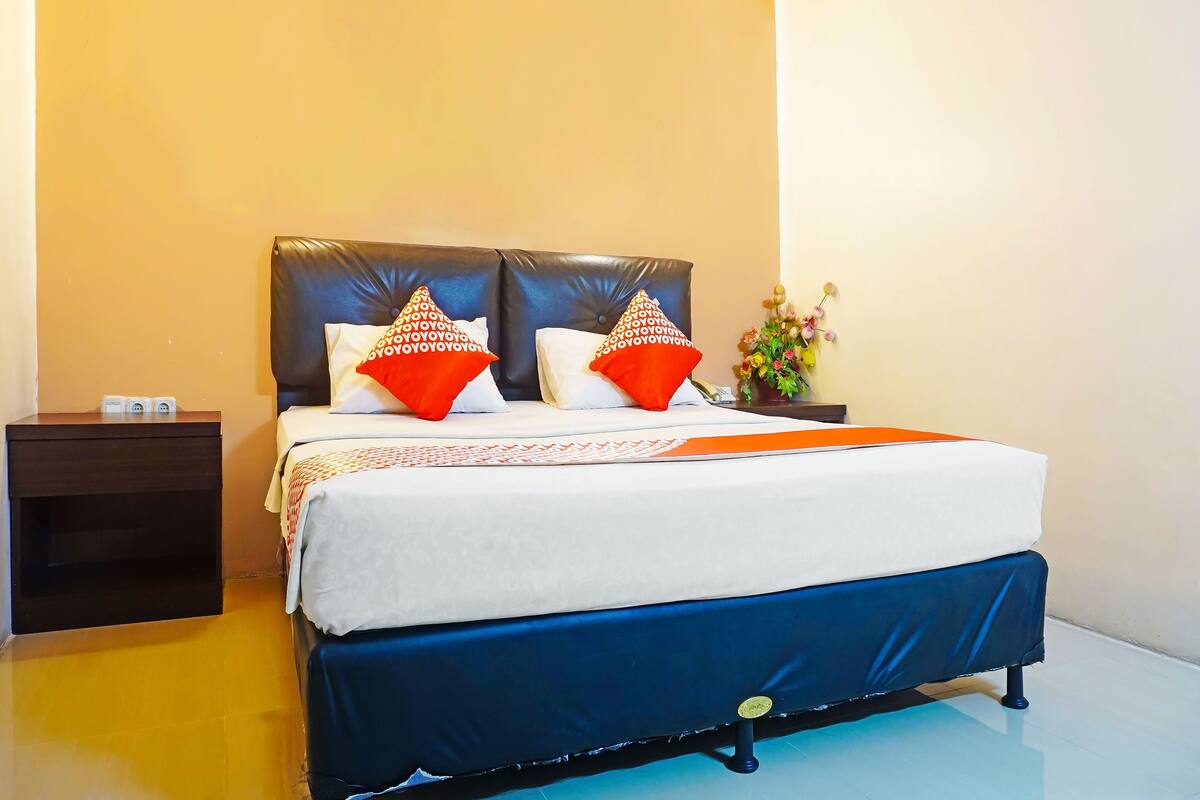 A hotel room with a bed, a nightstand, and a vase of flowers.