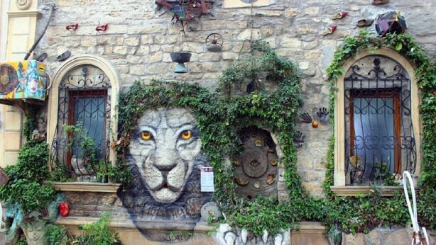 A building facade with a lion mural, stone walls, and decorative ironwork. - Qız Qalası Hotel (Baku)