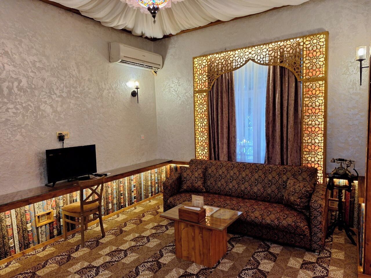 A living room with a patterned sofa, a wooden coffee table, a television, and a decorative wall panel.