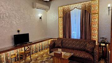 A living room with a patterned sofa, a wooden coffee table, a television, and a decorative wall panel.