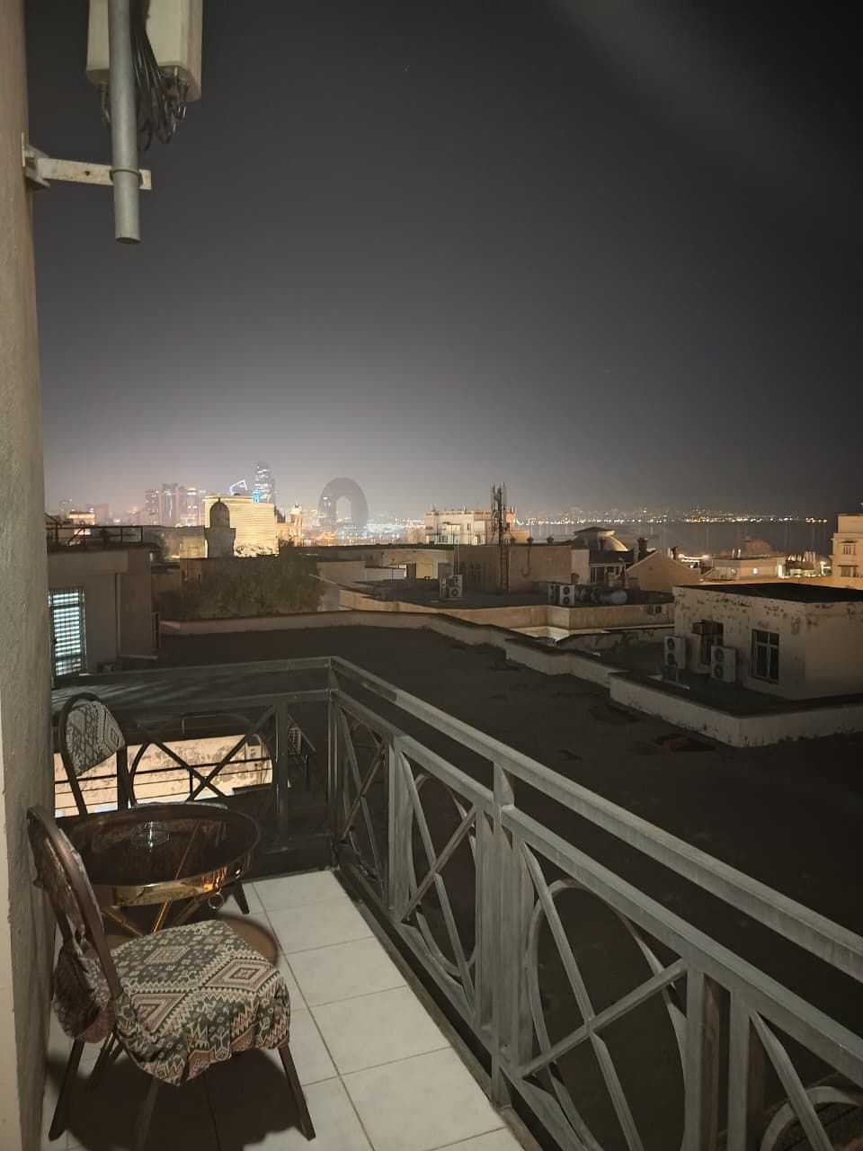 Un balcón con vista a un paisaje urbano nocturno, que incluye una estructura de arco distintiva.