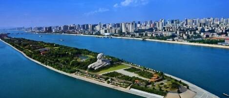 An aerial view of a coastal cityscape with a prominent island featuring a large stadium and landscaped areas.