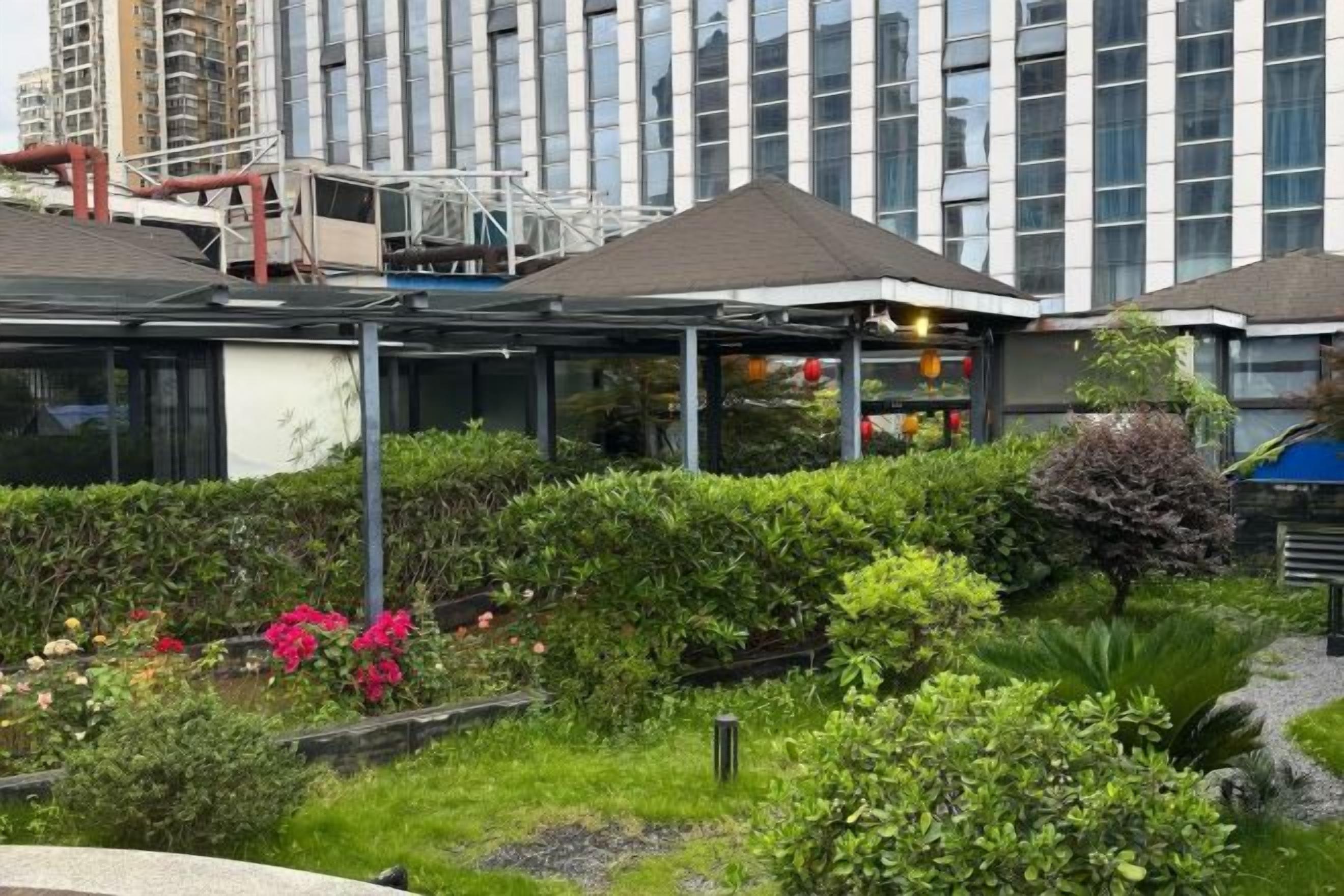 A hotel with a rooftop garden, a covered outdoor area, and a modern building in the background.