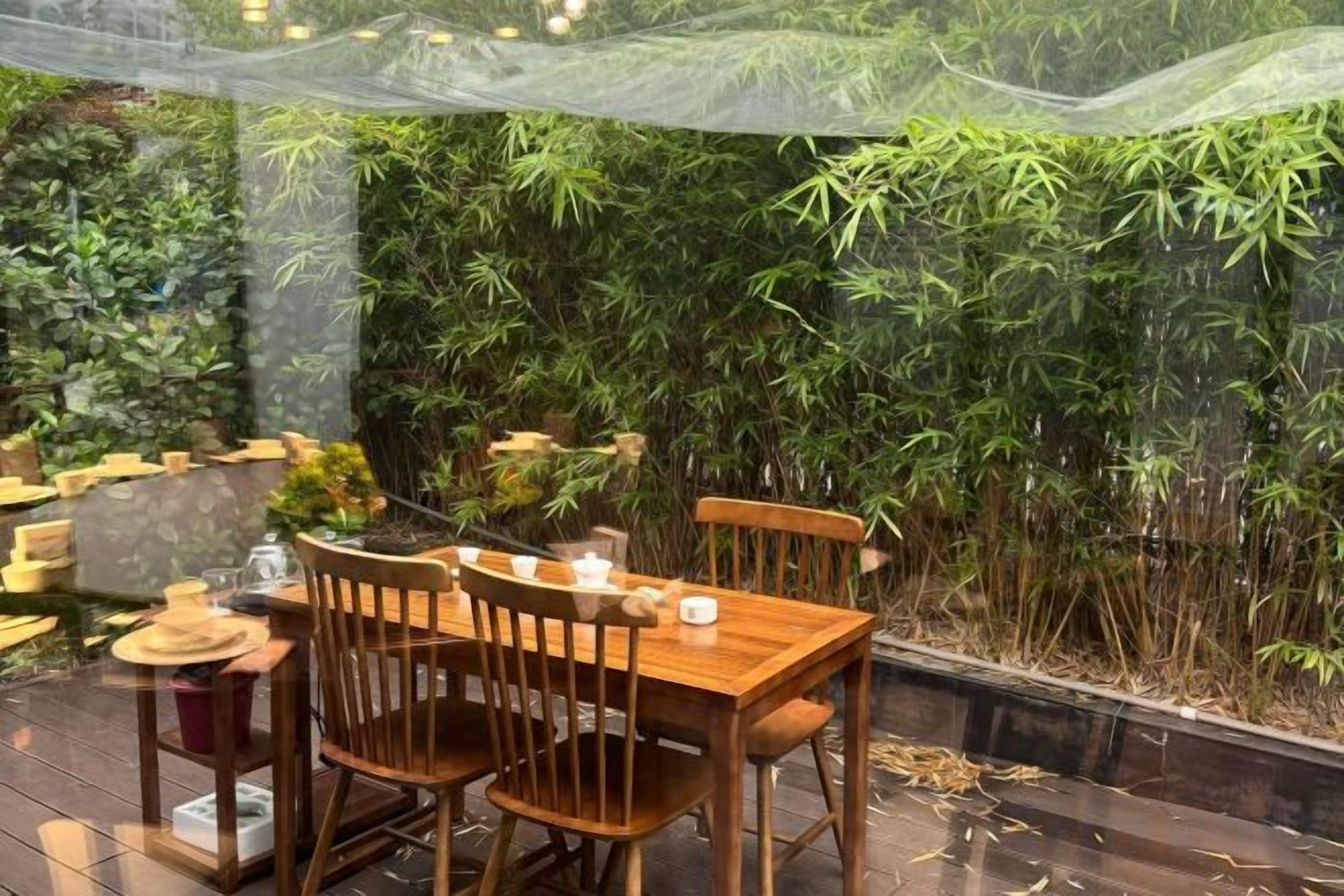 An outdoor dining area with a wooden table and chairs, surrounded by bamboo plants.