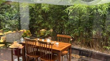 An outdoor dining area with a wooden table and chairs, surrounded by bamboo plants.