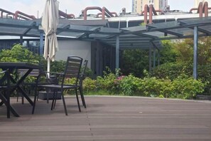 An outdoor patio with a table and chairs, a covered seating area, and a view of greenery and buildings in the background. - Ruiman International Hotel (Changsha)