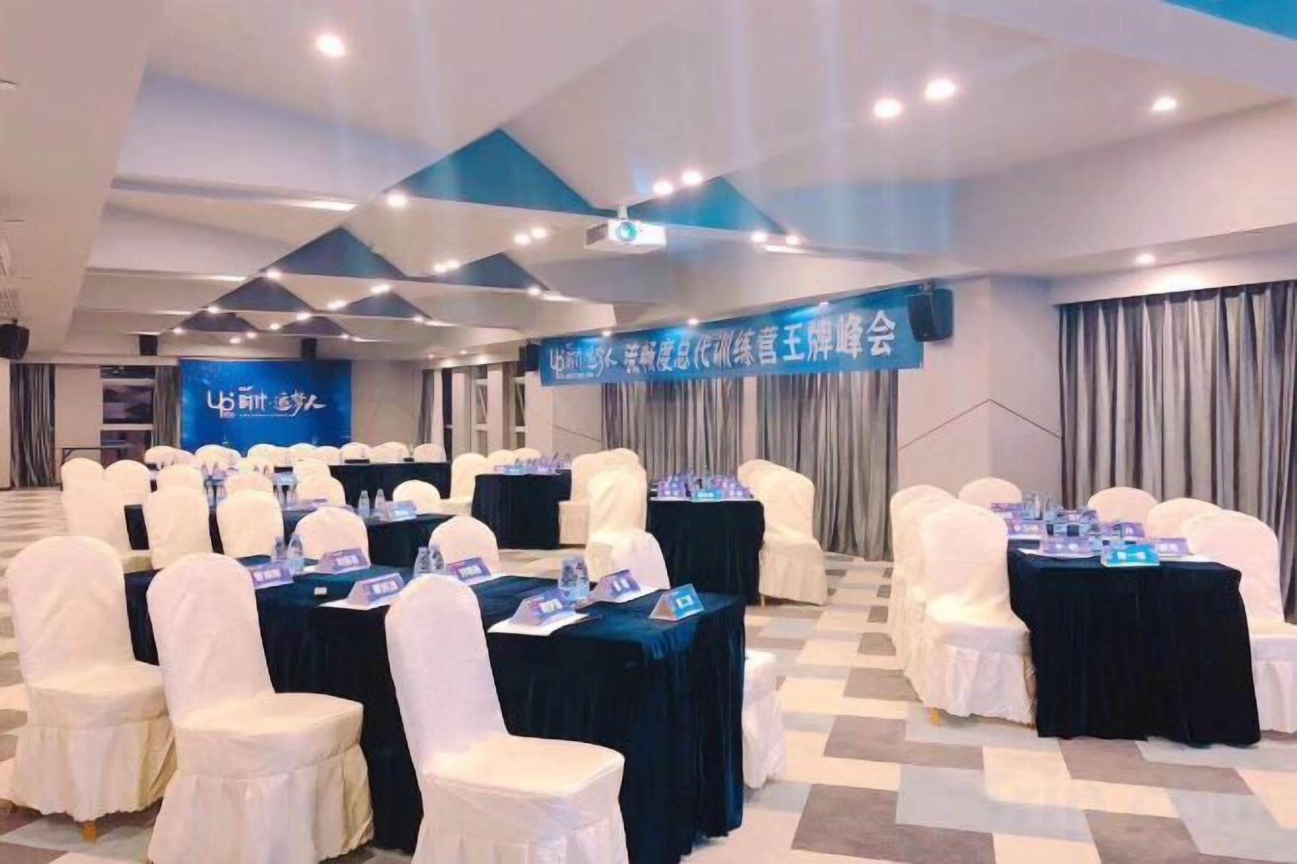 A conference room with rows of white chairs, tables with nameplates, and a banner with text.