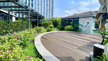 A modern outdoor area with a curved wooden deck, greenery, and a mural on a building.