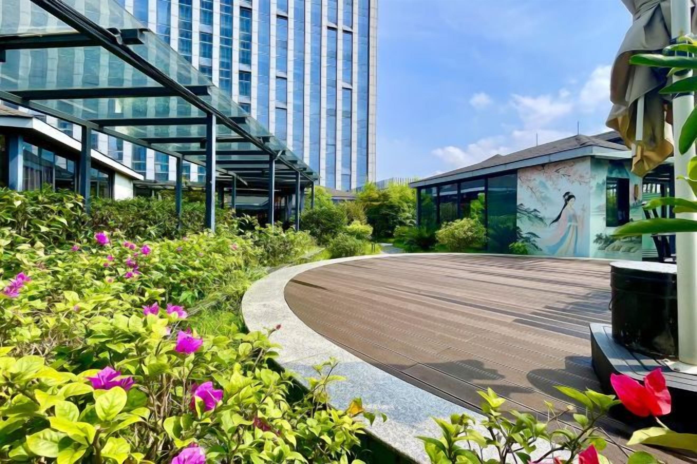 A modern building with a curved pathway, lush greenery, and a clear sky.
